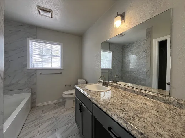 a bathroom with a granite countertop sink a toilet and shower