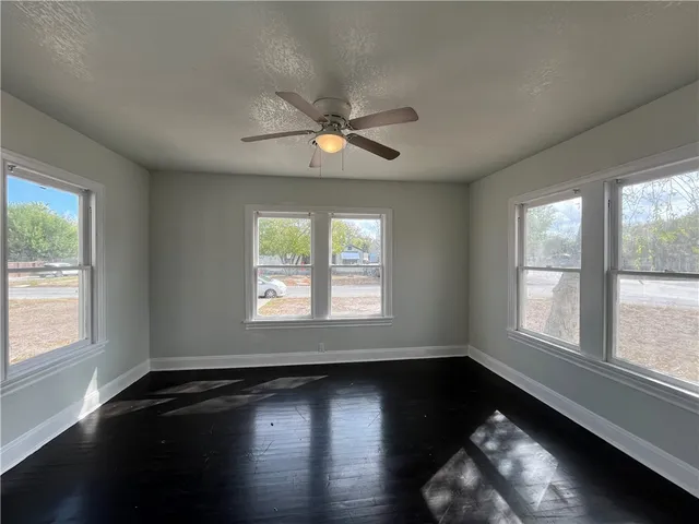 an empty room with wooden floor fan and windows