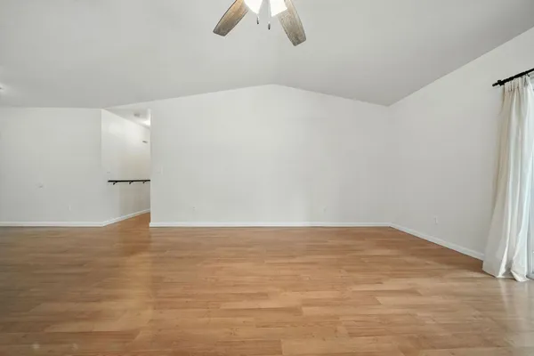 a view of an empty room with wooden floor and chandelier fan
