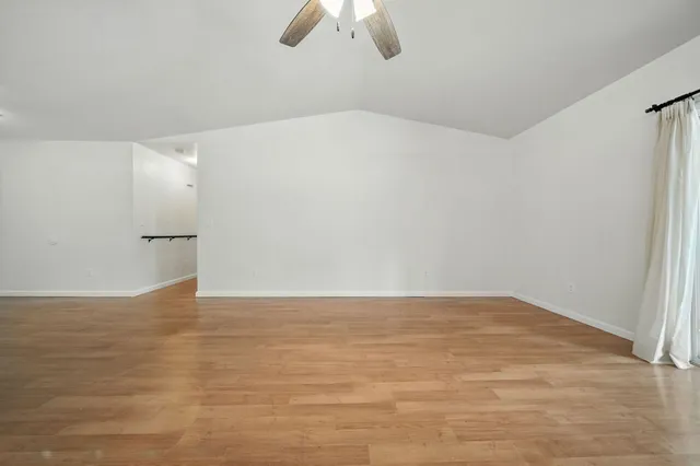 a view of an empty room with wooden floor and chandelier fan