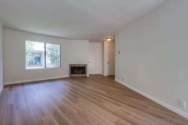 an empty room with wooden floor a fireplace and windows