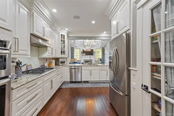 a kitchen with stainless steel appliances granite countertop a refrigerator a sink dishwasher a stove and white countertops with wooden floor
