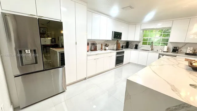 a large kitchen with a refrigerator a sink dishwasher a stove and white cabinets with wooden floor