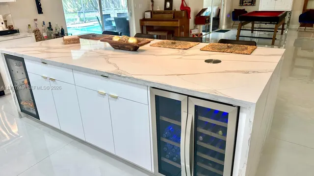 a room with kitchen island granite countertop a sink and white cabinets