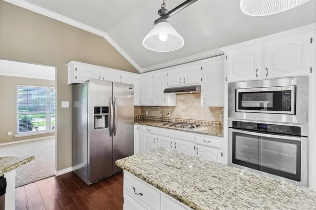 a kitchen with stainless steel appliances granite countertop a refrigerator a stove a sink and white cabinets with wooden floor