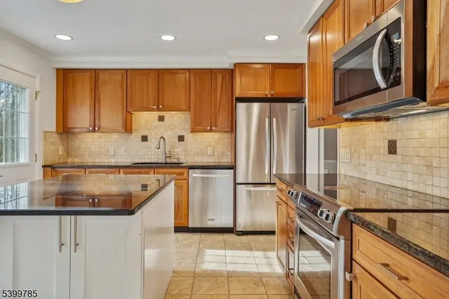 a kitchen with stainless steel appliances granite countertop a refrigerator a stove and a sink with wooden cabinets