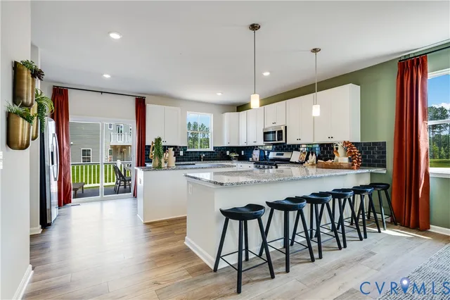 a kitchen with stainless steel appliances granite countertop a refrigerator a sink dishwasher a stove and white cabinets with wooden floor