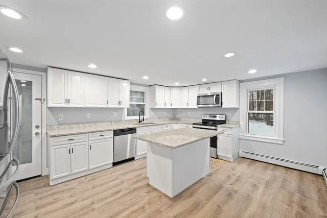 a kitchen with stainless steel appliances granite countertop a stove top oven a sink a refrigerator and white cabinets with wooden floor