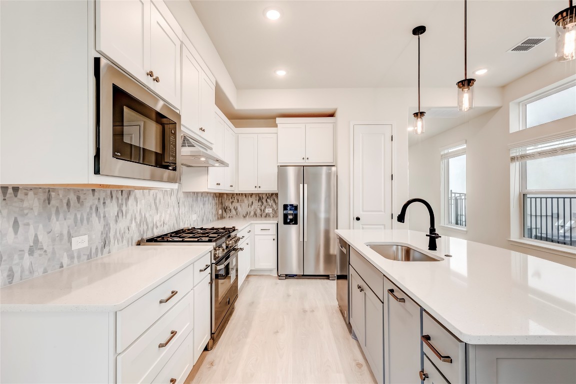 2008 Kit Circle Austin, TX 78758 - Photo 13 of 37 Kitchen featuring appliances with stainless steel finishes, a kitchen island with sink, decorative light fixtures, light stone countertops, and white cabinetry