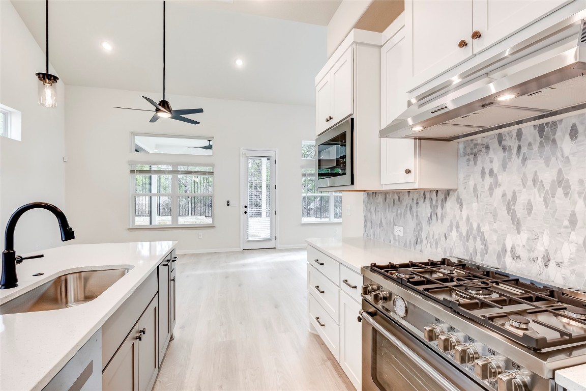 2008 Kit Circle Austin, TX 78758 - Photo 14 of 37 Kitchen with appliances with stainless steel finishes, under cabinet range hood, white cabinets, backsplash, and light stone countertops