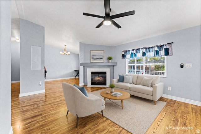 Vaulted ceiling living area featuring wood-finish flooring, a contemporary ceiling fan, and a fireplace with a mantel