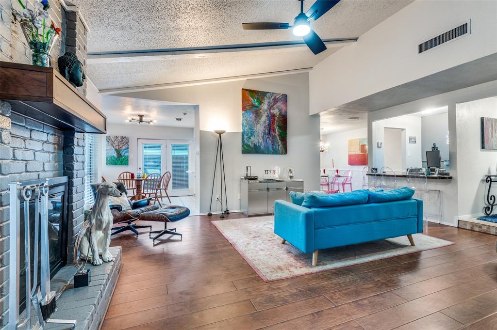 37 Merrie Circle Richardson, TX 75081 - Photo 10 of 28 Living area with vaulted ceiling, a textured ceiling, ceiling fan, a brick fireplace, and wood finished floors