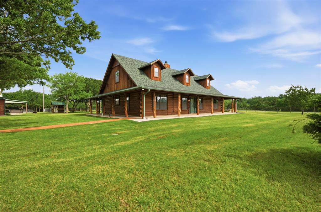 465 Emberson Ranch Road Pilot Point, TX 76258 - Photo 2 of 37 Log cabin exterior with a green shingle roof, multiple dormer windows, and a full-length covered porch featuring natural wood posts