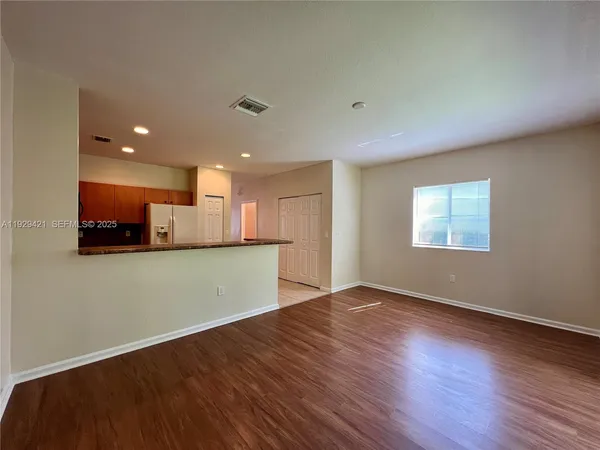 an empty room with wooden floor and a kitchen