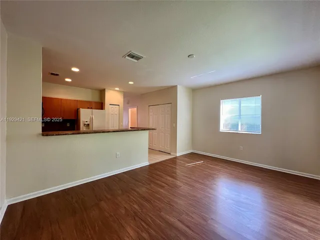 an empty room with wooden floor and a kitchen