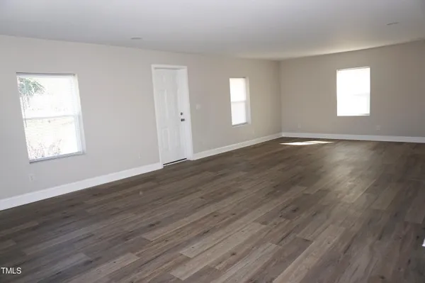 a view of an empty room with wooden floor and window