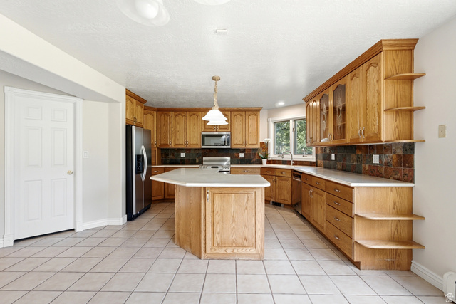 3535 Homestead Road Park City, UT 84098 - Photo 14 of 81 Kitchen featuring wood cabinetry, an angled island with a light-toned countertop, a tile backsplash, stainless steel appliances, and tile flooring