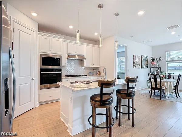 a kitchen with stainless steel appliances kitchen island granite countertop a stove a refrigerator a oven a dining table and chairs with wooden floor