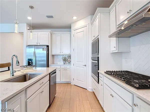 a kitchen with a sink stove a refrigerator and white cabinets with wooden floor