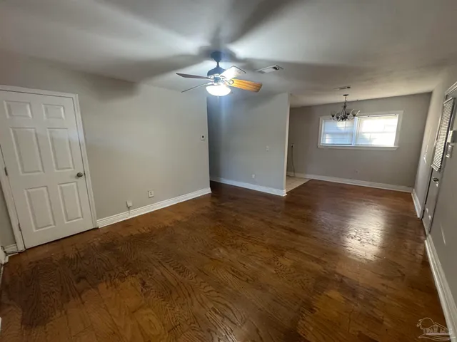 an empty room with wooden floor chandelier fan and windows