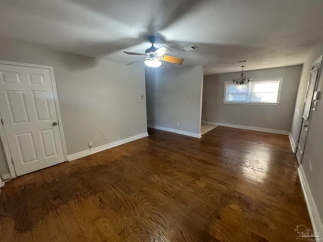 an empty room with wooden floor chandelier fan and windows