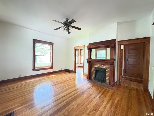 a view of an empty room with wooden floor fireplace and a window