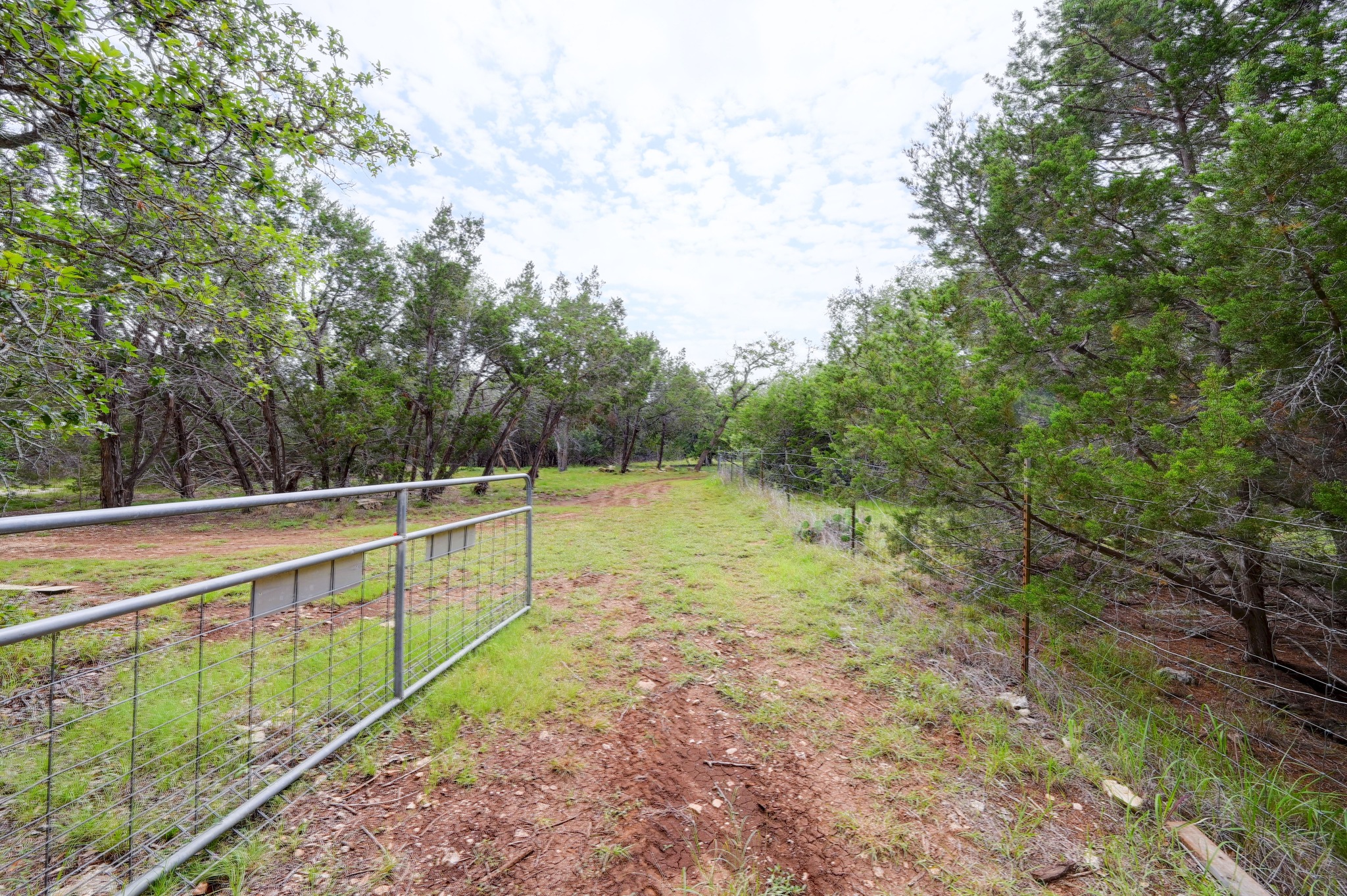 231 North Rainbow Ranch Road Wimberley, TX 78676 - Photo 31 of 40 A private, gated entrance opens to a secluded natural landscape with abundant mature trees.