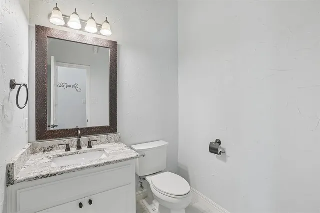 a bathroom with a granite countertop sink vanity mirror and toilet