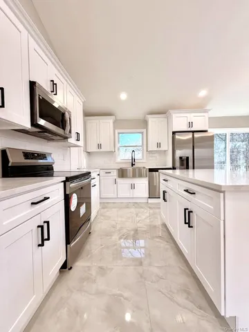 a kitchen with stainless steel appliances granite countertop a stove top oven a sink and white cabinets