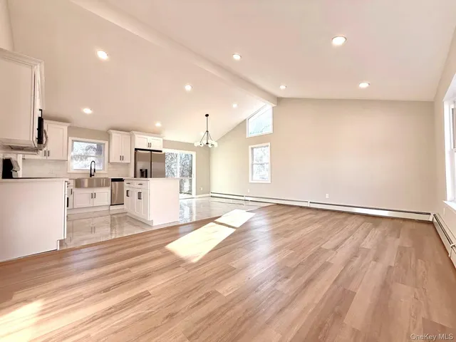 a view of empty room with wooden floor and kitchen
