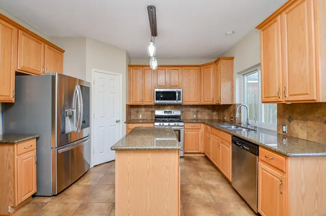 a kitchen with granite countertop a refrigerator a sink a stove top oven and a dishwasher