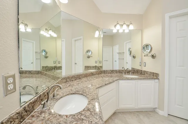 a bathroom with a granite countertop double vanity sink mirror and shower