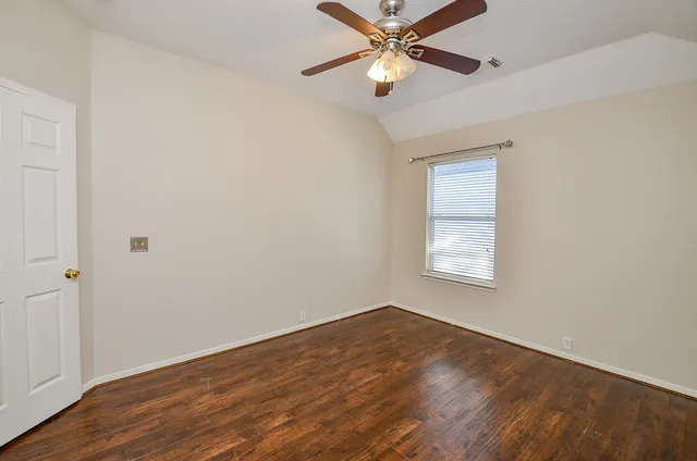 an empty room with wooden floor fan and windows