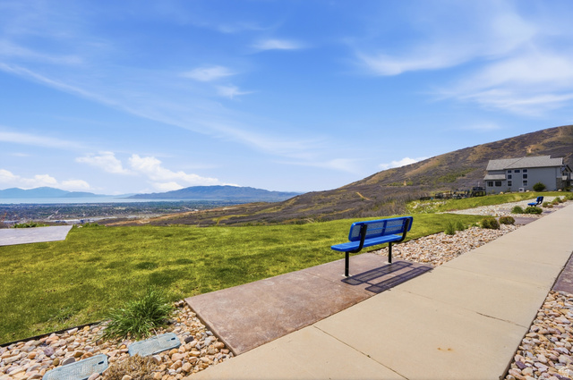 2007 Fielding Hill Lane Draper, UT 84020 - Photo 51 of 83 Expansive green space featuring a concrete pathway, blue metal bench, decorative rock landscaping, and distant mountain and water scenery