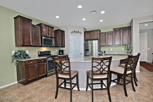 a kitchen with stainless steel appliances kitchen island granite countertop a stove a refrigerator a sink a dining table and chairs