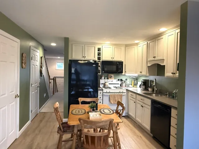 a kitchen with stainless steel appliances granite countertop a sink a stove a refrigerator cabinets and a dining table with wooden floor