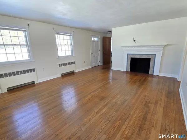 an empty room with wooden floor fireplace and windows