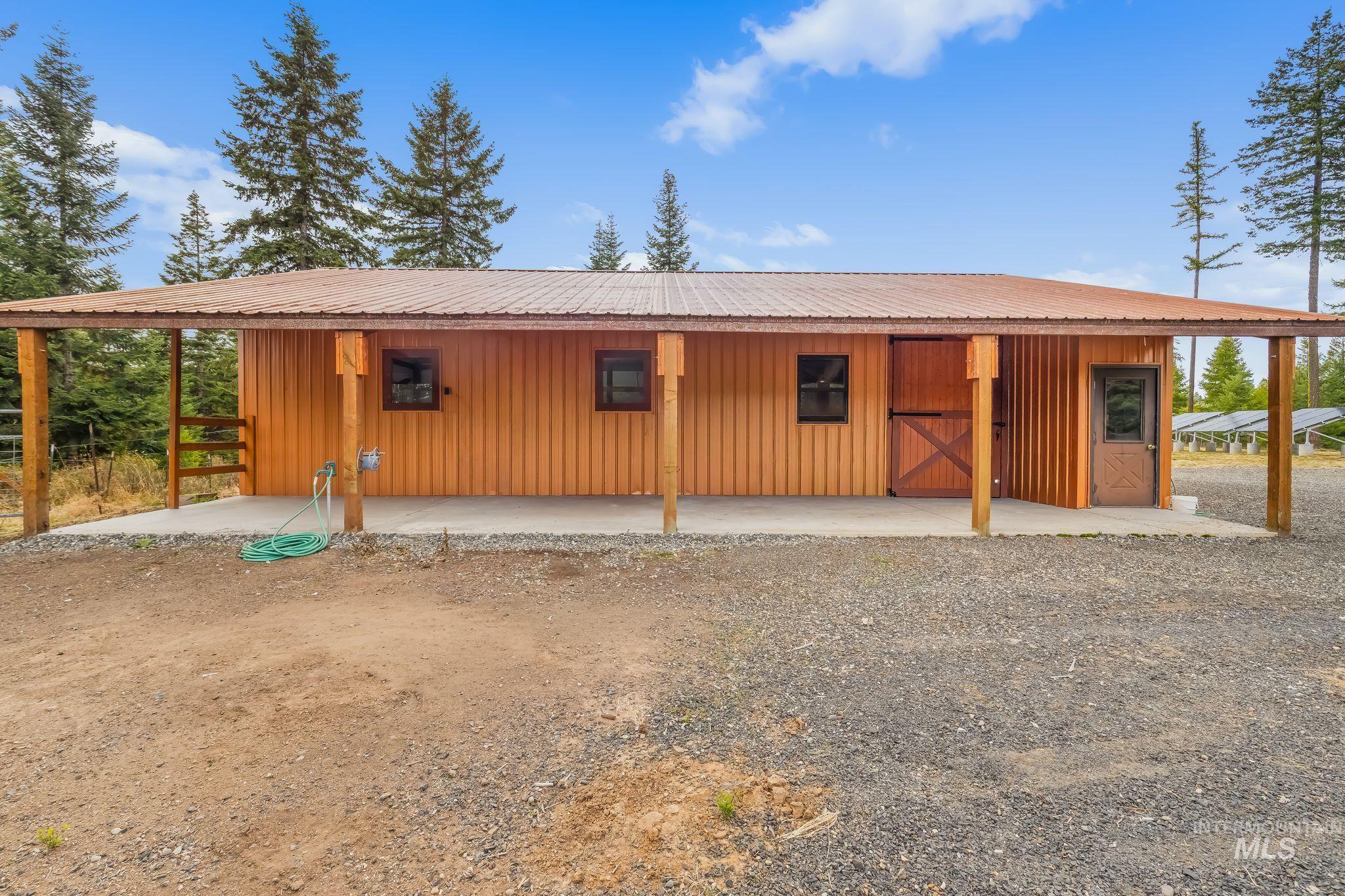 3989 East Mountain Road Anatone, WA 99401 - Photo 28 of 49 Wood-sided outbuilding with a metal roof, featuring a covered concrete patio, sliding barn door, and a paneled entry door