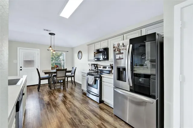 a kitchen with stainless steel appliances granite countertop a refrigerator a stove and a dining table with wooden floor