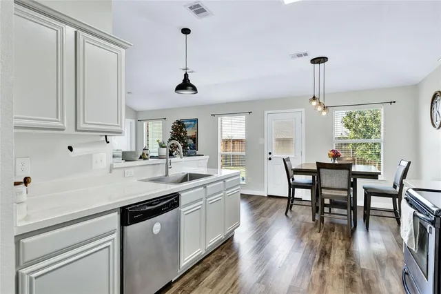 a kitchen with stainless steel appliances granite countertop a sink a stove a dining table chairs and white cabinets