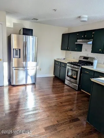 a kitchen with stainless steel appliances granite countertop a stove a refrigerator and a wooden floor