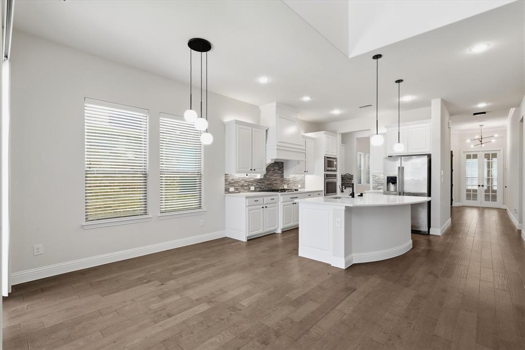 2433 Mare Road Carrollton, TX 75010 - Photo 37 of 37 Open-concept floor plan featuring wood flooring, a kitchen with a curved island, white cabinetry, and stainless steel appliances, pendant lighting and breakfast area.