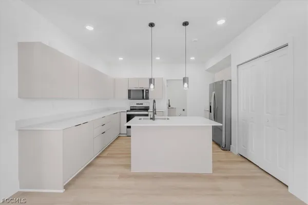 a kitchen with stainless steel appliances a refrigerator a sink dishwasher a stove and white cabinets with wooden floor