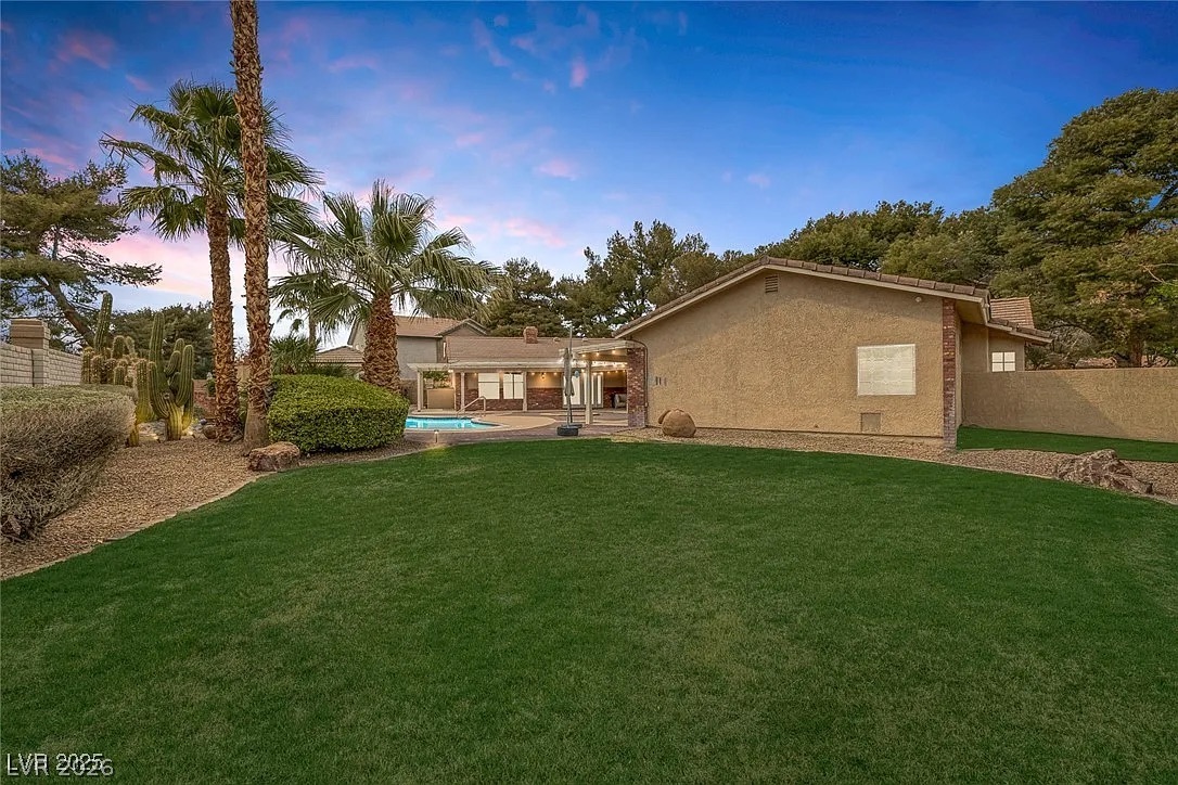 9 Quail Run Road Henderson, NV 89014 - Photo 46 of 57 An inviting backyard oasis offers a sparkling pool, generous lawn, and mature desert landscaping under an evening sky.