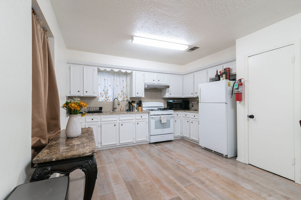 1106 Saucedo Street Austin, TX 78721 - Photo 14 of 34 Kitchen featuring white appliances, under cabinet range hood, light wood-type flooring, white cabinets, and a textured ceiling