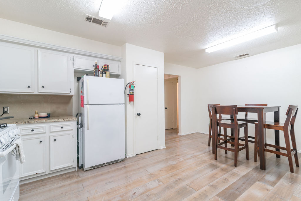 1106 Saucedo Street Austin, TX 78721 - Photo 15 of 34 Kitchen featuring white appliances, light wood-type flooring, a textured ceiling, white cabinets, and light stone counters