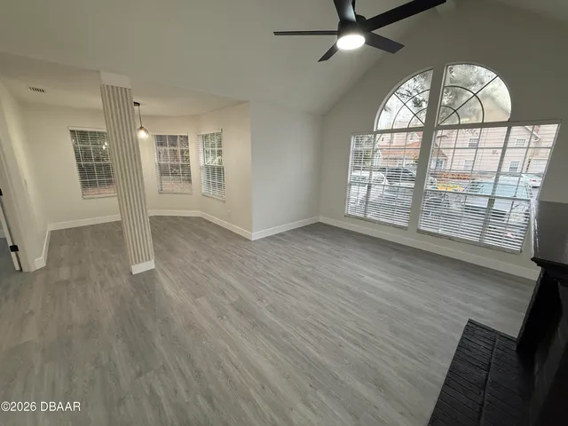 an empty room with wooden floor fan and windows