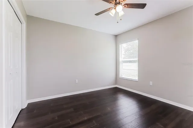 an empty room with wooden floor chandelier fan and windows