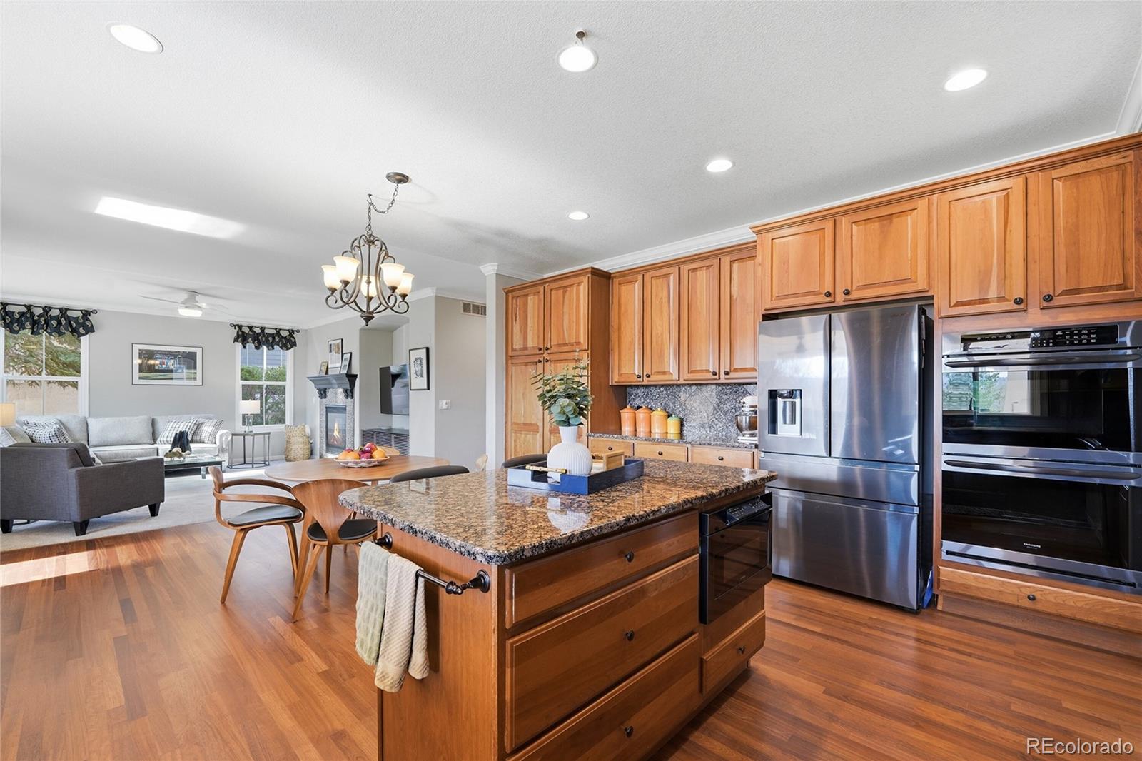 8967 Hunters Way Highlands Ranch, CO 80129 - Photo 20 of 50 a kitchen with granite countertop a refrigerator stove a dining table and chairs with wooden floor