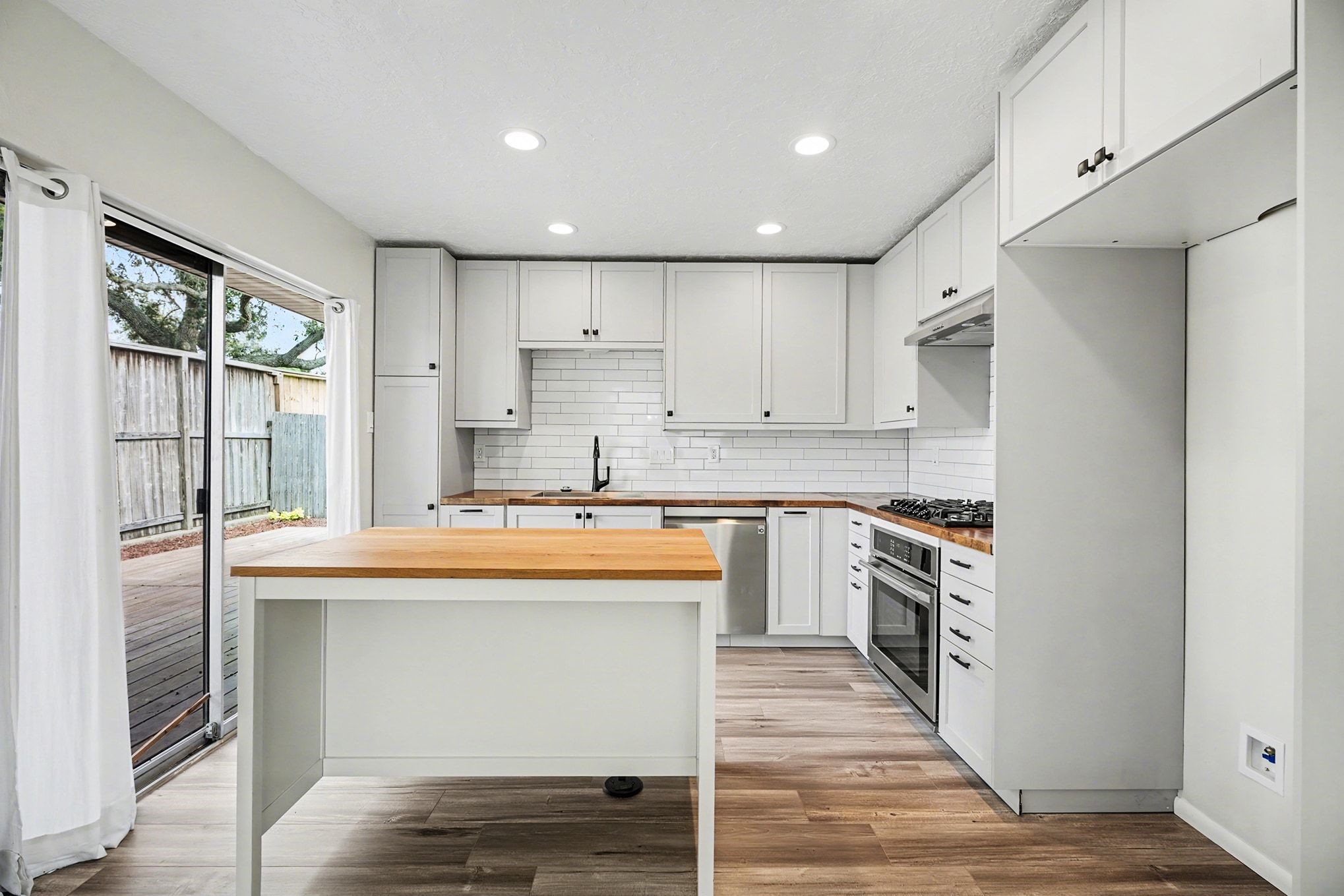 1723 Linfield Way Houston, TX 77058 - Photo 5 of 21 This kitchen features modern white cabinetry, a subway tile backsplash, and stainless steel appliances. It includes a central island with wood countertops and opens to a deck through sliding glass doors, providing ample natural light and a connection to outdoor space.